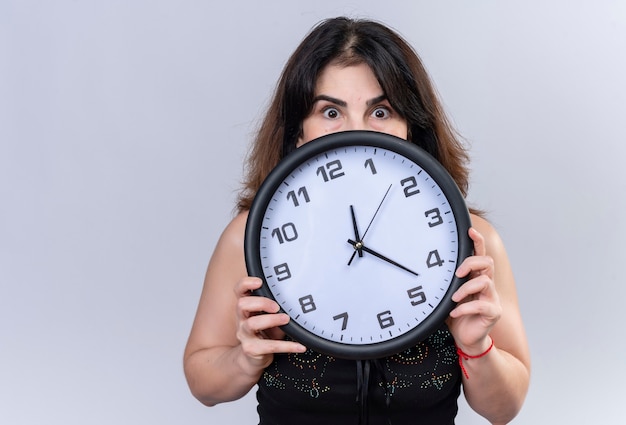 Foto gratuita mujer bonita en blusa negra asustada escondiéndose detrás del reloj