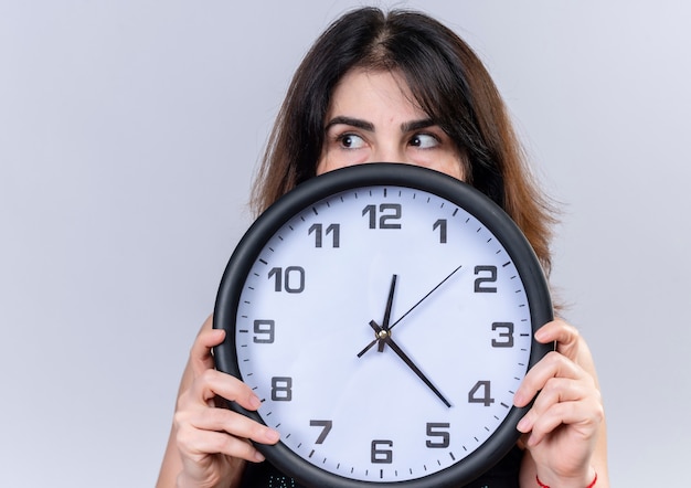 Mujer bonita en blusa negra escondida detrás del reloj mirando además