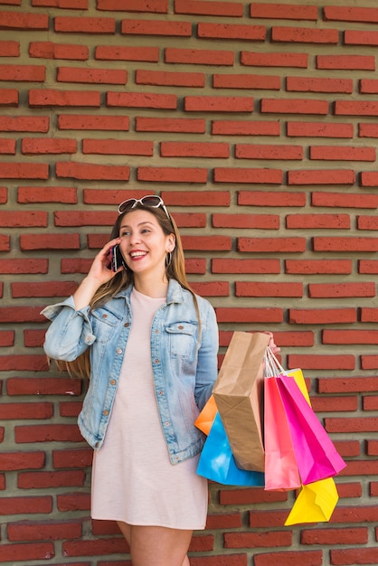 Mujer bonita con bolsas brillantes hablando por teléfono en la pared de ladrillo