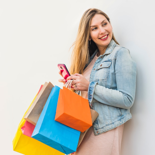 Mujer bonita con los bolsos de compras brillantes usando smartphone
