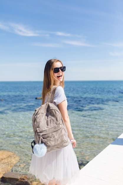 Mujer bonita con cabello largo está caminando con bolsa cerca del mar