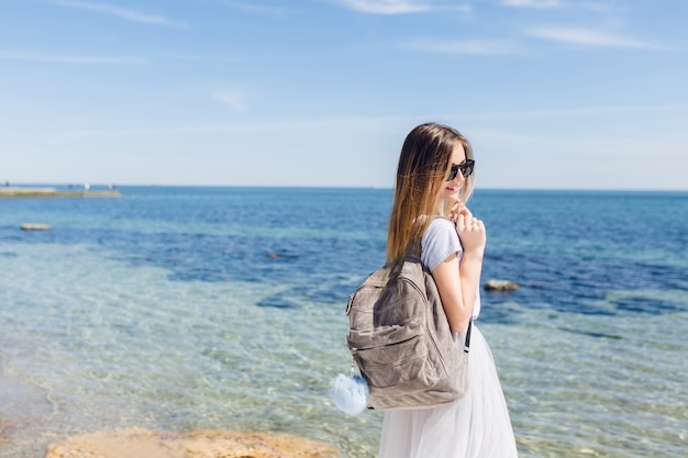 Mujer bonita con cabello largo está caminando con bolsa cerca del mar
