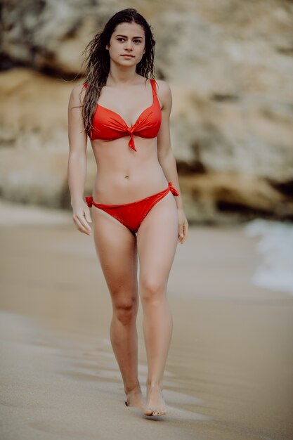 Mujer bonita caminando por una playa de arena en bikini rojo y disfrutando del sol