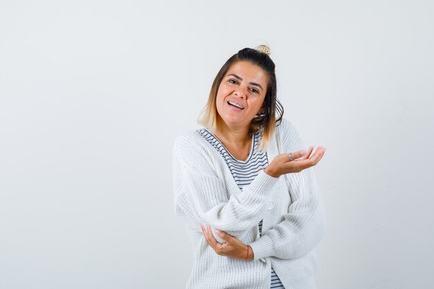 Mujer bonita en camiseta, chaqueta de punto extendiendo la palma a un lado y mirando confundido