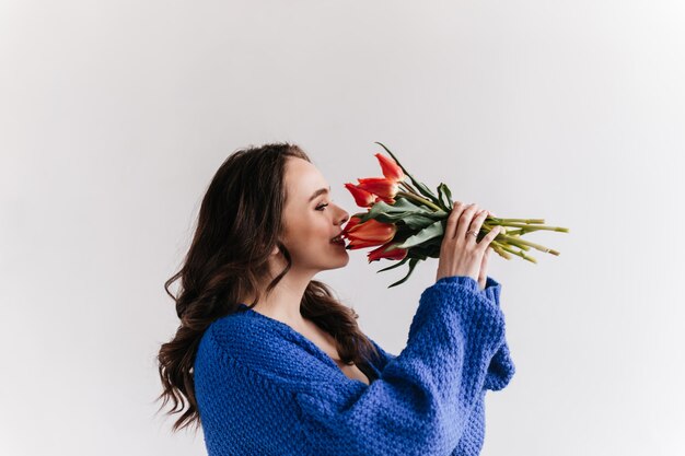 Una mujer bonita en cárdigan de lana azul huele a tulipanes. Señora morena feliz tiene ramo sobre fondo blanco aislado.