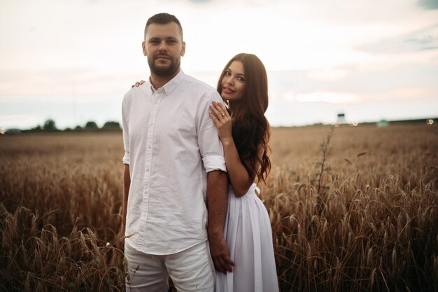 Mujer bonita caucásica con cabello largo ondulado oscuro en vestido blanco abraza con hombre hermoso en camiseta blanca y pantalones cortos