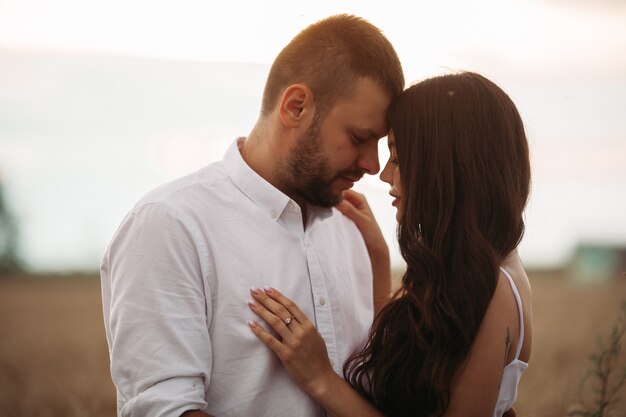 Mujer bonita caucásica con cabello largo ondulado oscuro en vestido blanco abraza con hombre hermoso en camiseta blanca y pantalones cortos