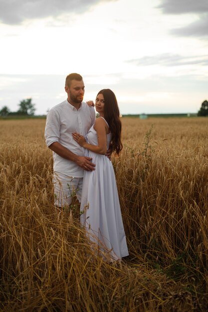 Mujer bonita caucásica con cabello largo ondulado oscuro en vestido blanco abraza con hombre hermoso en camiseta blanca y pantalones cortos