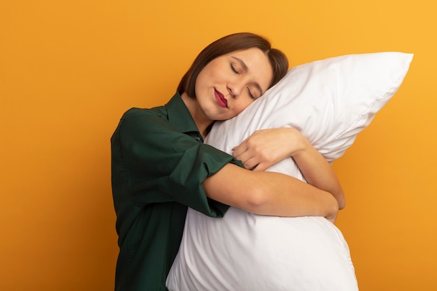 Mujer bonita caucásica soñolienta sostiene y pone la cabeza sobre la almohada en naranja