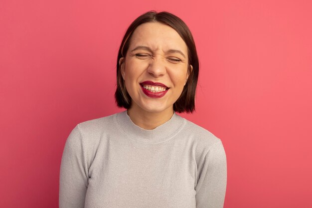 Mujer bonita caucásica sonriente complacida se encuentra con los ojos cerrados en rosa