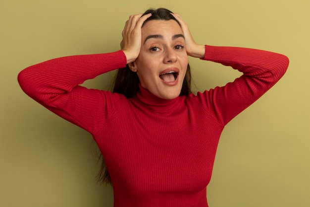 Mujer bonita caucásica sorprendida con las manos en la cabeza en verde oliva