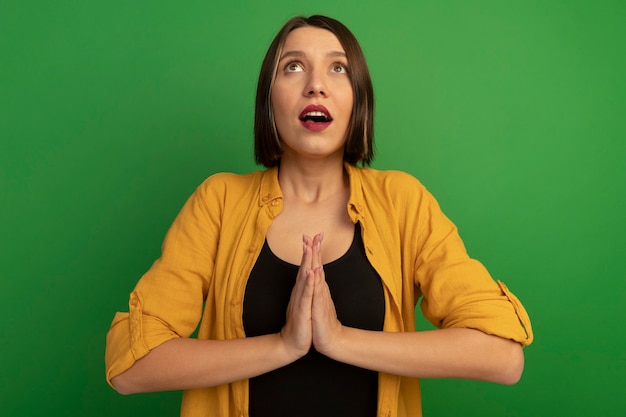 Foto gratuita mujer bonita caucásica sorprendida toma las manos juntas y mira hacia arriba en verde