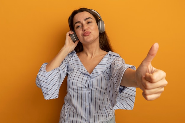 Foto gratuita mujer bonita complacida en auriculares thumbs up aislado en pared naranja