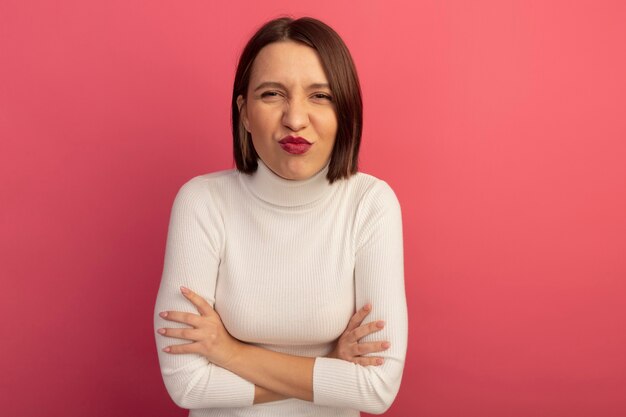 Mujer bonita complacida se encuentra con los brazos cruzados aislados en la pared rosa