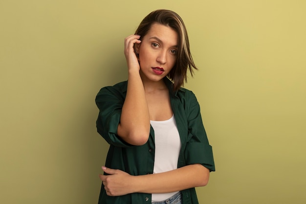 Foto gratuita mujer bonita confiada sostiene la mano cerca de la cabeza aislada en la pared verde oliva