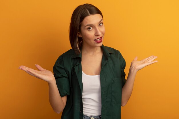 Mujer bonita confiada tiene las manos abiertas aisladas en la pared naranja