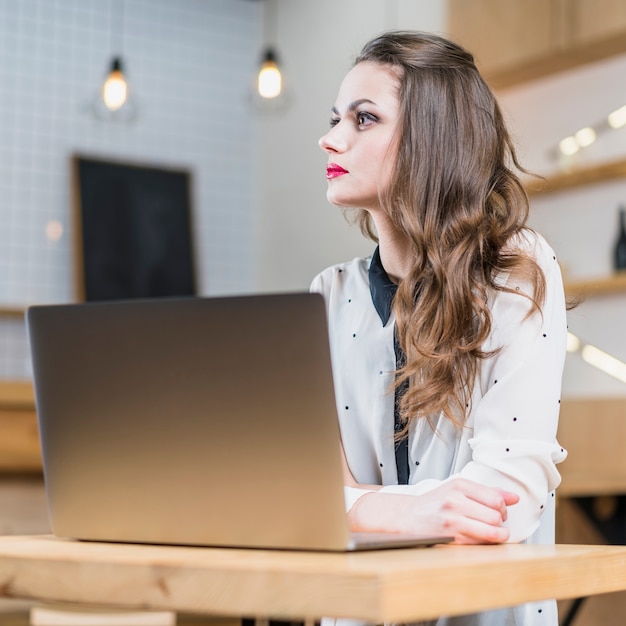 Foto gratuita mujer bonita contemplada que se sienta delante de la computadora portátil abierta