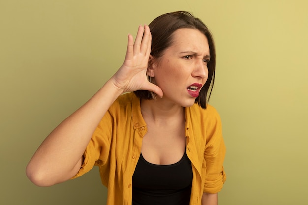 Mujer bonita despistada tiene la mano detrás de la oreja aislada en la pared verde oliva