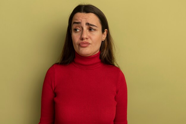 Mujer bonita disgustada mira al lado aislado en la pared verde oliva