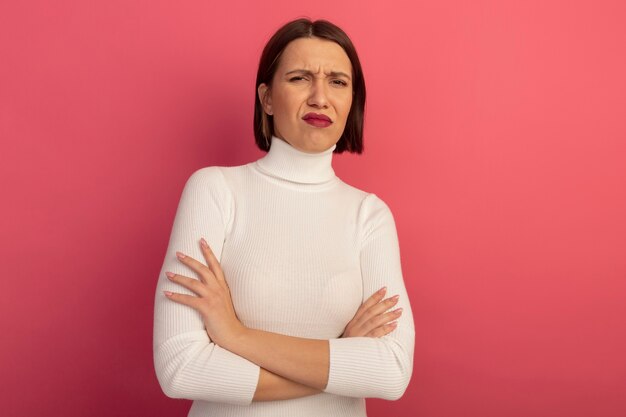 Mujer bonita disgustada de pie con los brazos cruzados aislado en la pared rosa