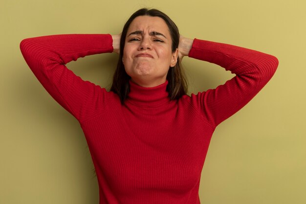 Mujer bonita disgustada pone las manos en la cabeza aislada en la pared verde oliva