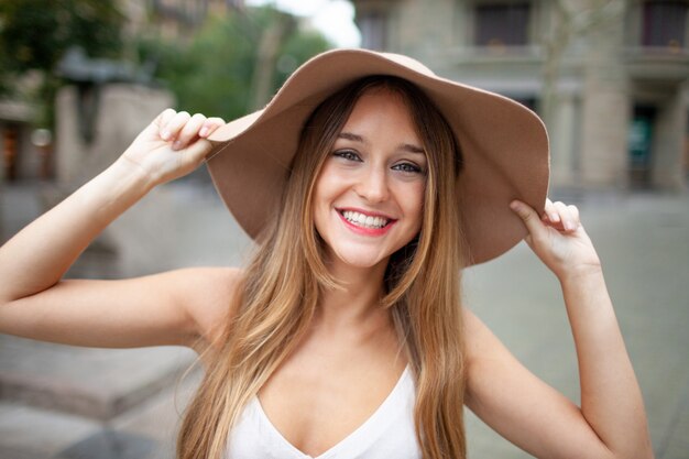 Mujer bonita emocionada alegre que sostiene el borde del sombrero