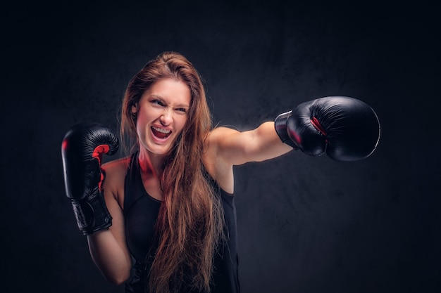 Una mujer bonita y emocionada está demostrando su golpe con un grito, usando guantes de boxeo.