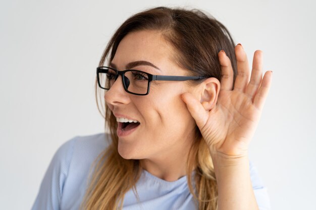 Mujer bonita emocionada que lleva a cabo la mano cerca de la oreja