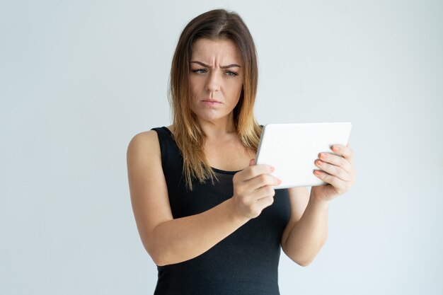 Mujer bonita escéptica que lee noticias en la tableta. Señora navegando en tableta.