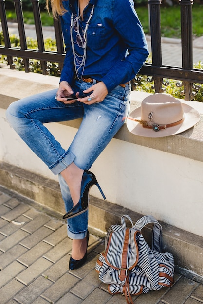Mujer bonita con estilo joven sosteniendo un teléfono, vestida con jeans y camisa de mezclilla