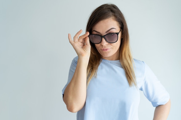 Mujer bonita con estilo que ajusta gafas de sol y que mira la cámara.