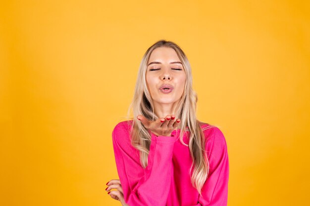 Mujer bonita europea en blusa rosa sobre pared amarilla