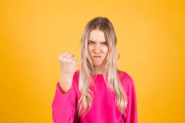 Mujer bonita europea en blusa rosa sobre pared amarilla