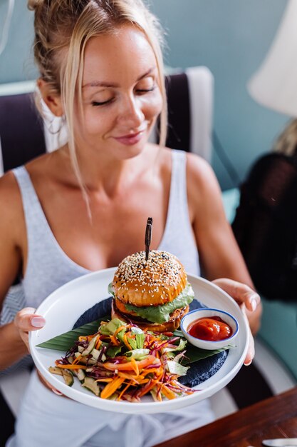 Mujer bonita europea hambrienta de jugosa hamburguesa en café de verano