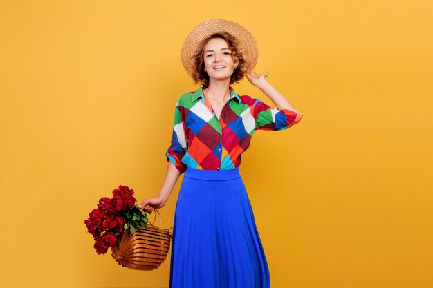 Mujer bonita europea en vestido azul con ramo de flores sobre fondo amarillo. Sombrero de copa. Humor de verano.