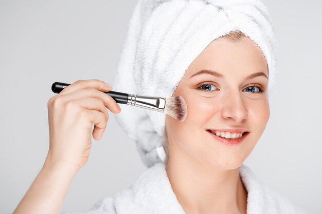 Mujer bonita feliz aplicar maquillaje con pincel, usar toalla de baño