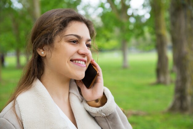 Mujer bonita feliz que invita a smartphone en parque