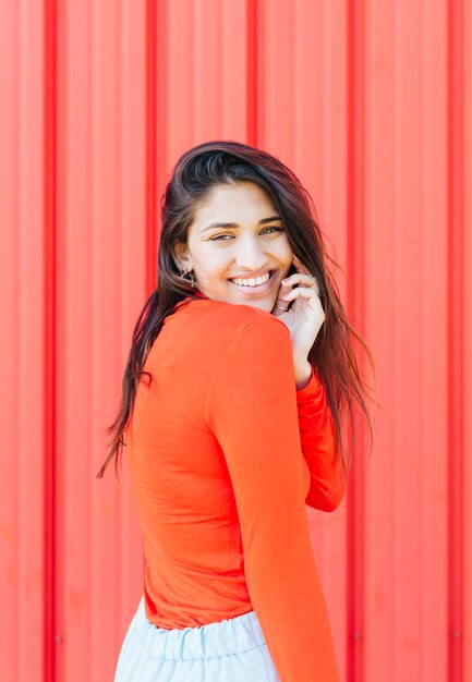 Mujer bonita feliz que presenta delante de fondo rojo