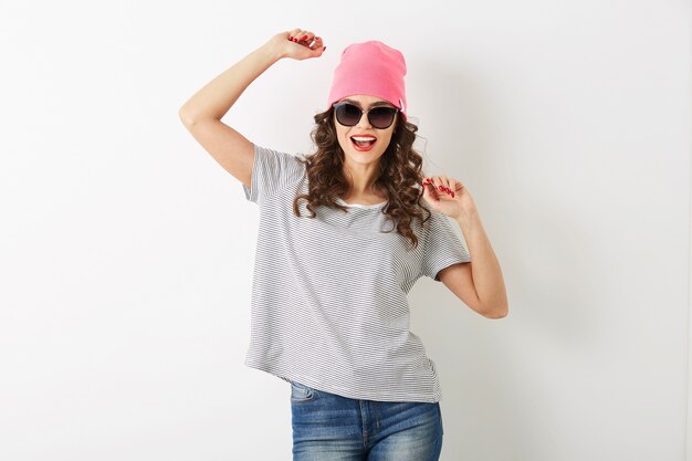 Mujer bonita hipster con sombrero rosa, gafas de sol, bailando feliz, cara sonriente, cabello largo, estado de ánimo positivo, emocional, traje de estilo hipster, tendencia de moda de verano, jeans y camiseta a rayas, aislado