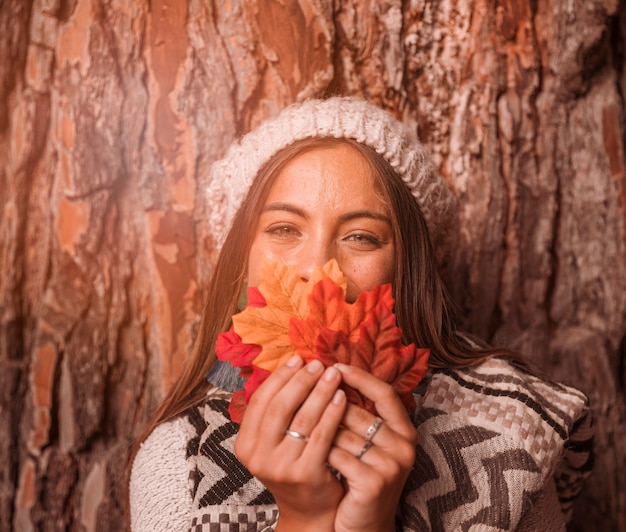 Mujer bonita con hojas de otoño cerca de árbol