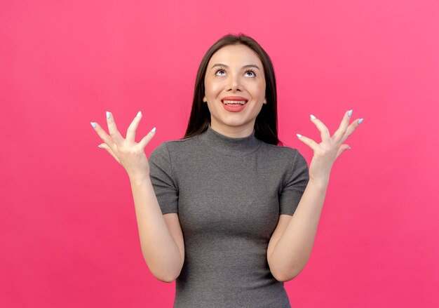 Mujer bonita joven alegre mirando hacia arriba y manteniendo las manos en el aire aislado sobre fondo rosa