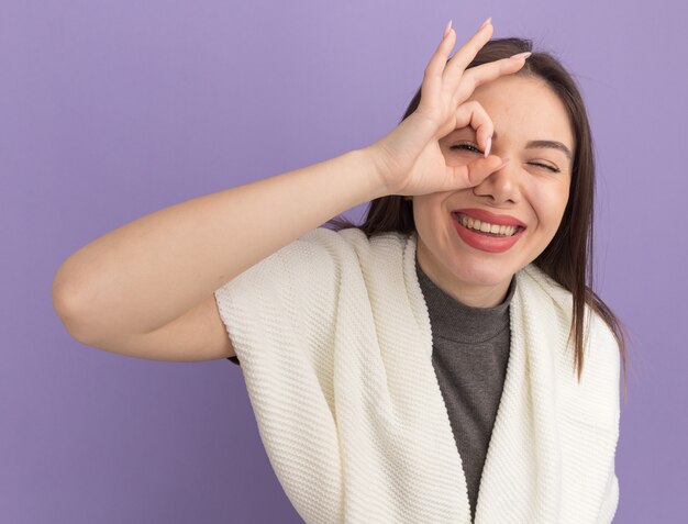 Mujer bonita joven alegre que hace gesto de la mirada mirando al frente guiñando un ojo aislado en la pared púrpura