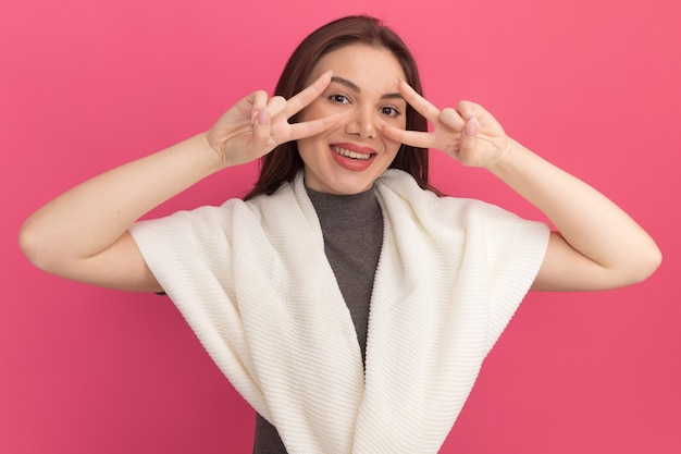 Mujer bonita joven alegre que muestra símbolos de signo v cerca de los ojos