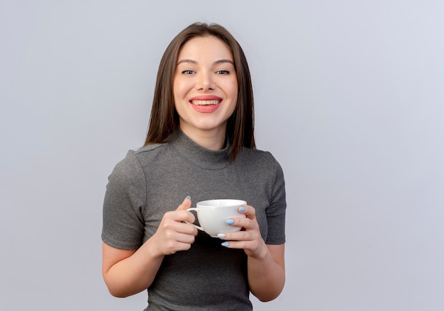 Mujer bonita joven alegre sosteniendo la taza mirando a la cámara aislada sobre fondo blanco con espacio de copia