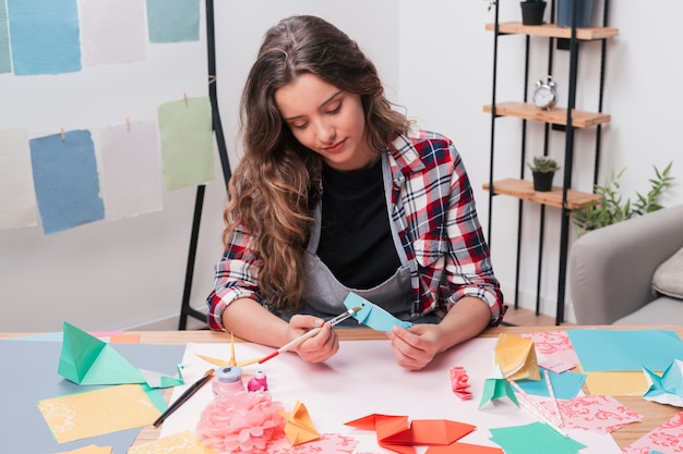 Mujer bonita joven del artista que pinta pescados del origami usando la brocha