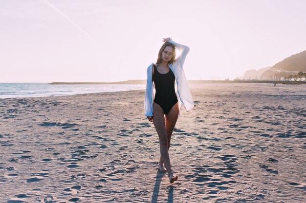 Mujer bonita joven en bikini en la playa al atardecer