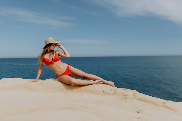 Mujer bonita joven en bikini rojo y sombrero de paja en la colina de piedra