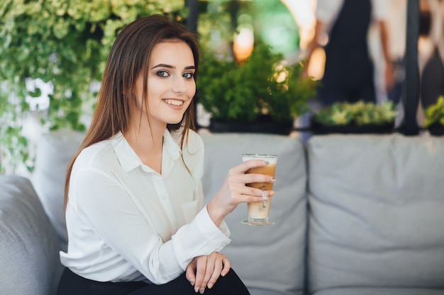 Mujer bonita joven con café en sus manos con una camisa blanca sentado en la oficina