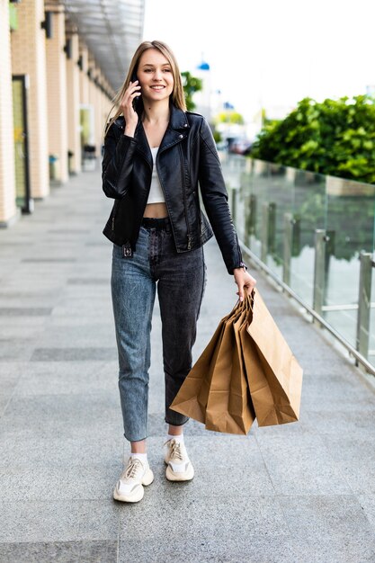 Mujer bonita joven en la calle con bolsas de la compra hablando por teléfono móvil