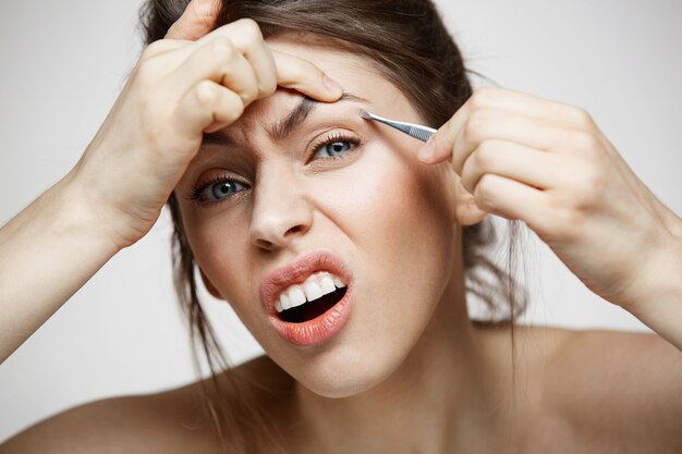 La mujer bonita joven con las cejas perfectas de la piel limpia pellizca la cara divertida. Belleza y spa.